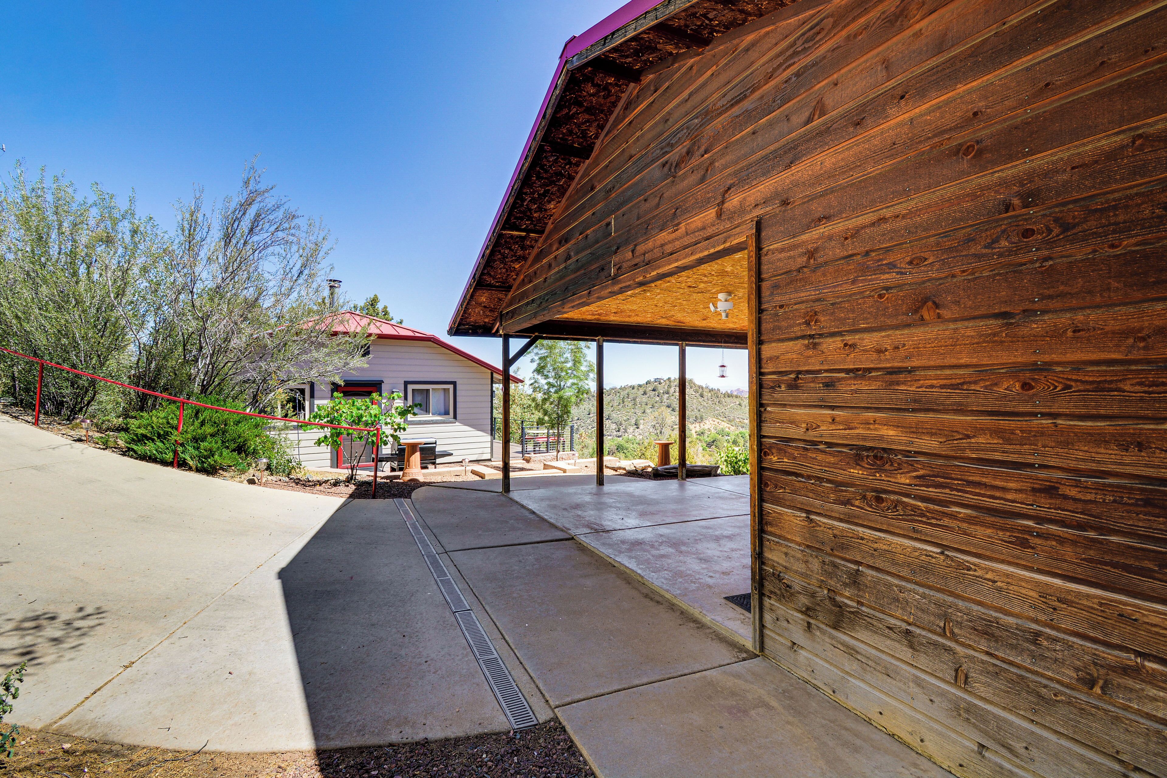 A wooden exterior wall, a concrete pathway, and a building with a red roof in the background.