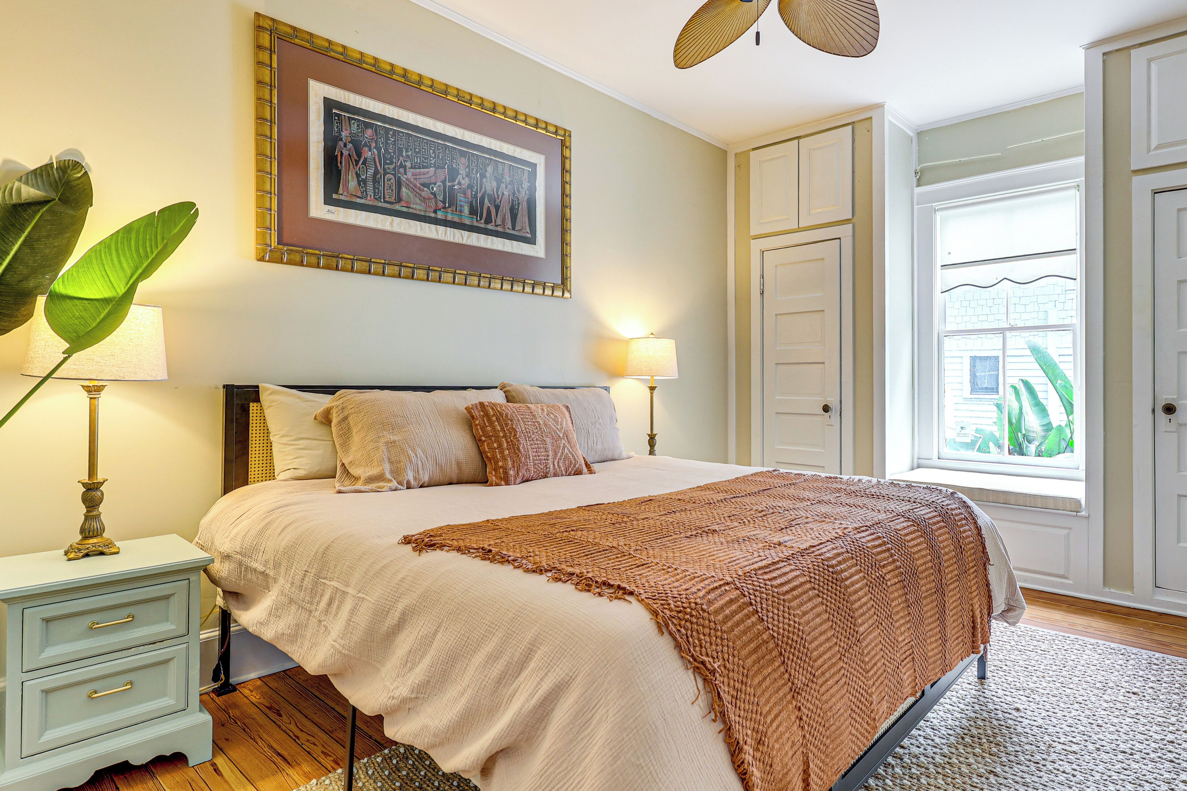 A bedroom with a bed, bedside lamps, a framed picture on the wall, and a window with a view.