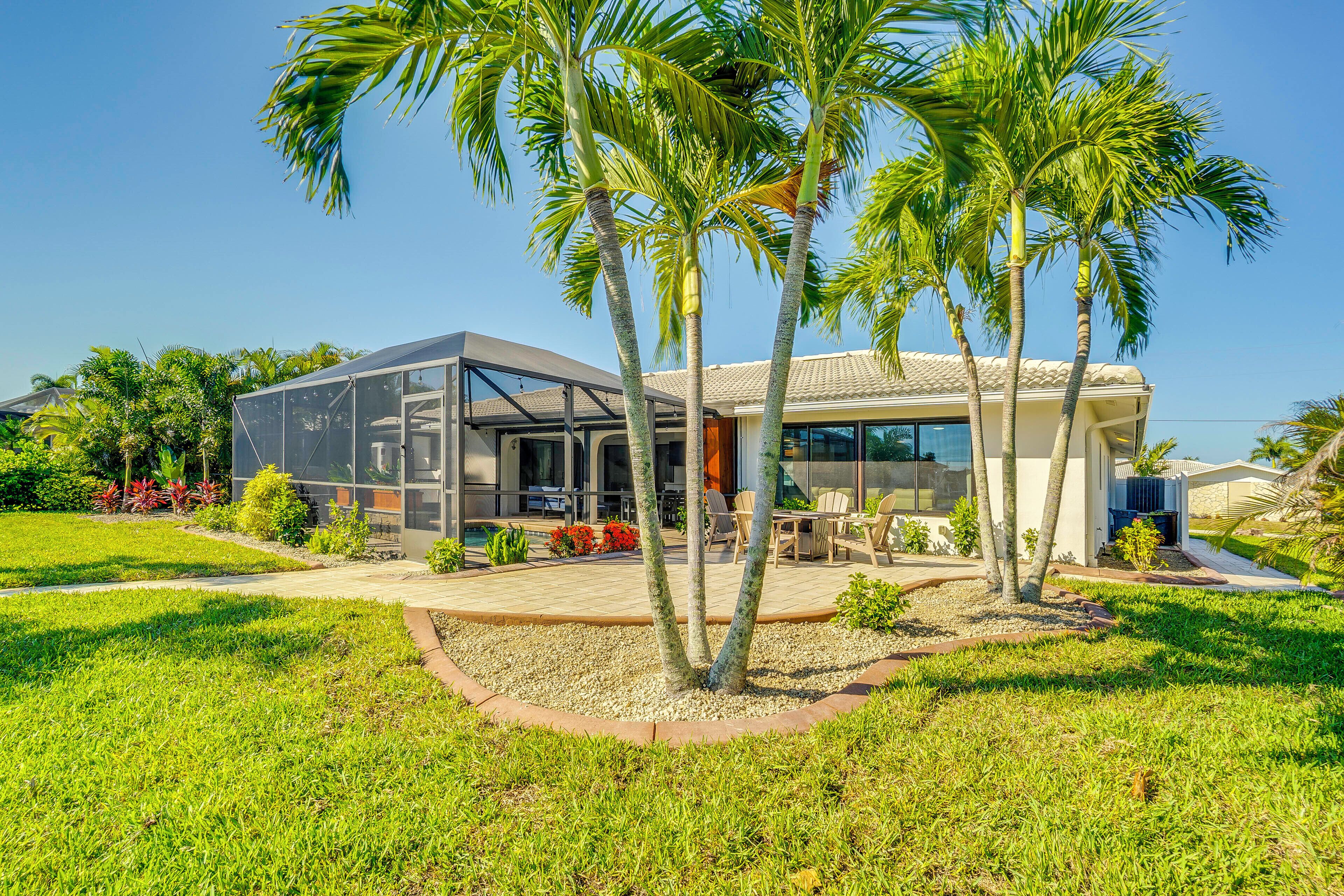 A modern house with a glass facade, outdoor seating, and palm trees.