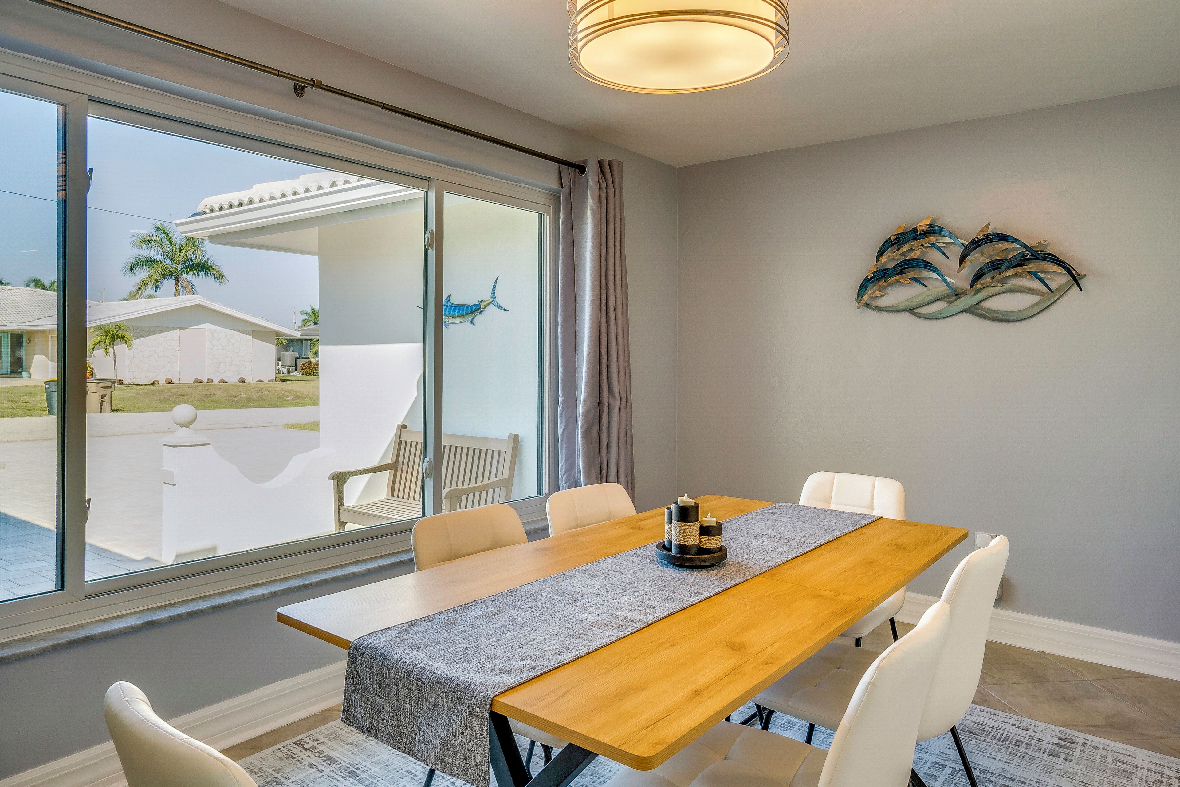 A dining area with a wooden table, white chairs, a grey table runner, and a view of the outside.