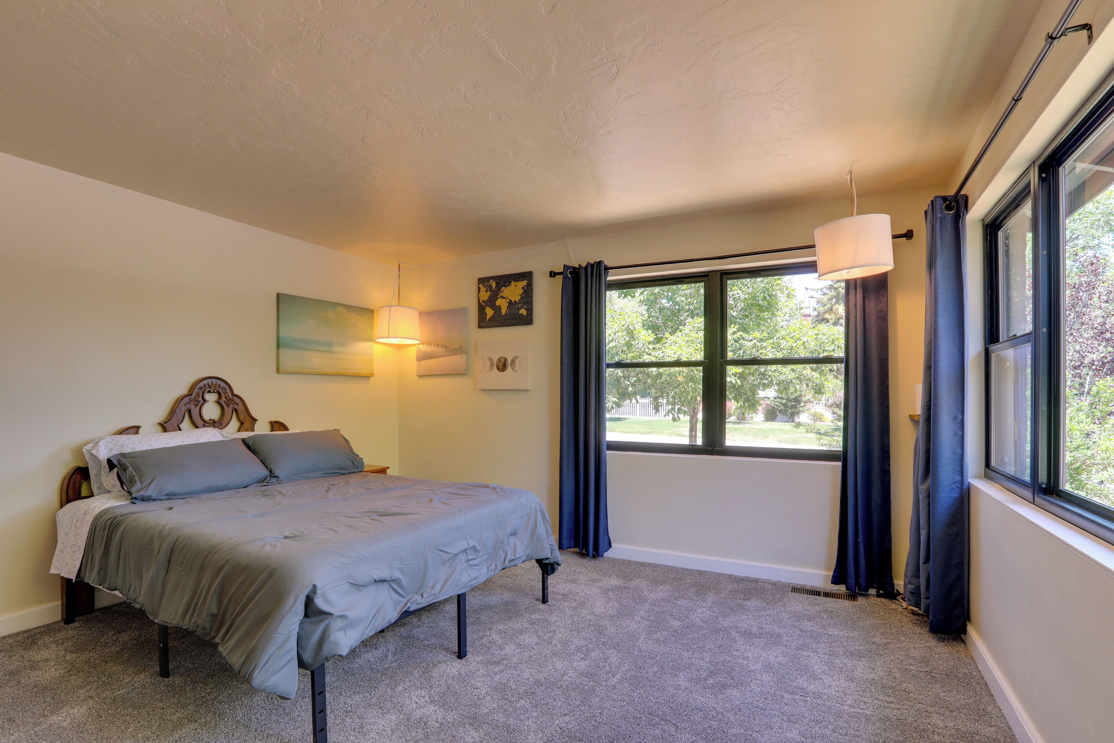 A bedroom with a bed, a window with curtains, a hanging light, and a world map on the wall.