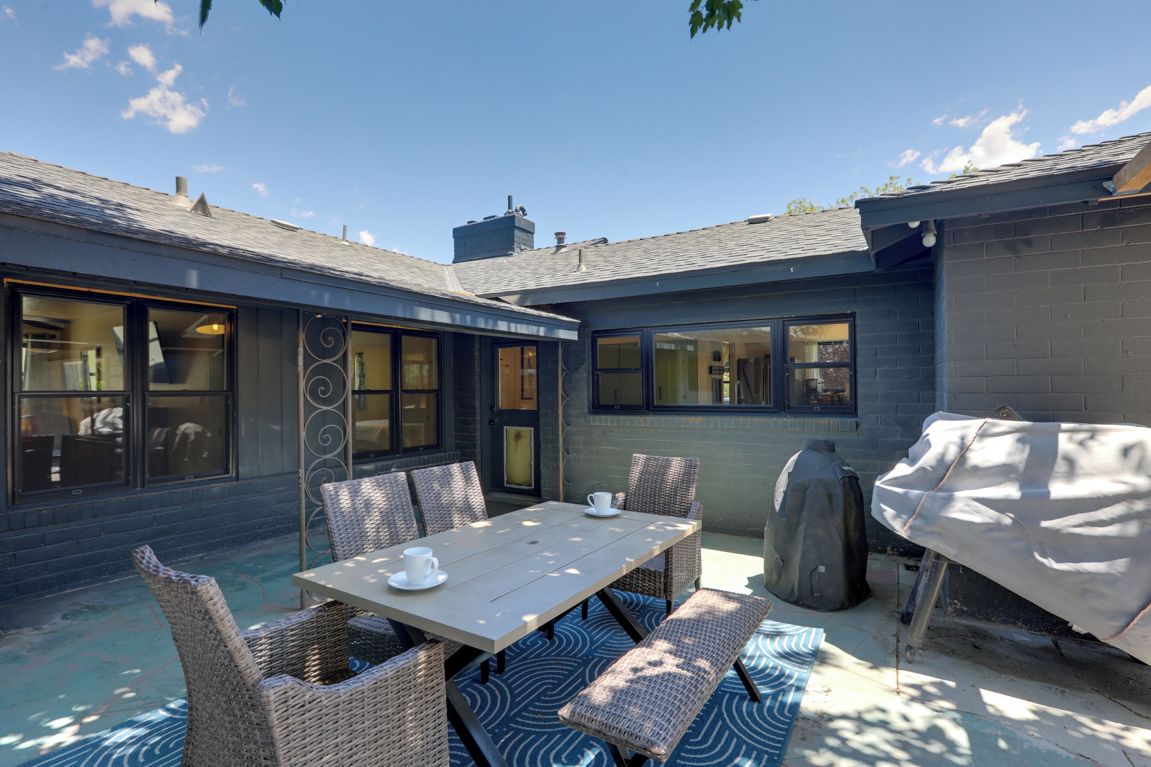 An outdoor patio with a table and chairs, a covered grill, and a covered object.