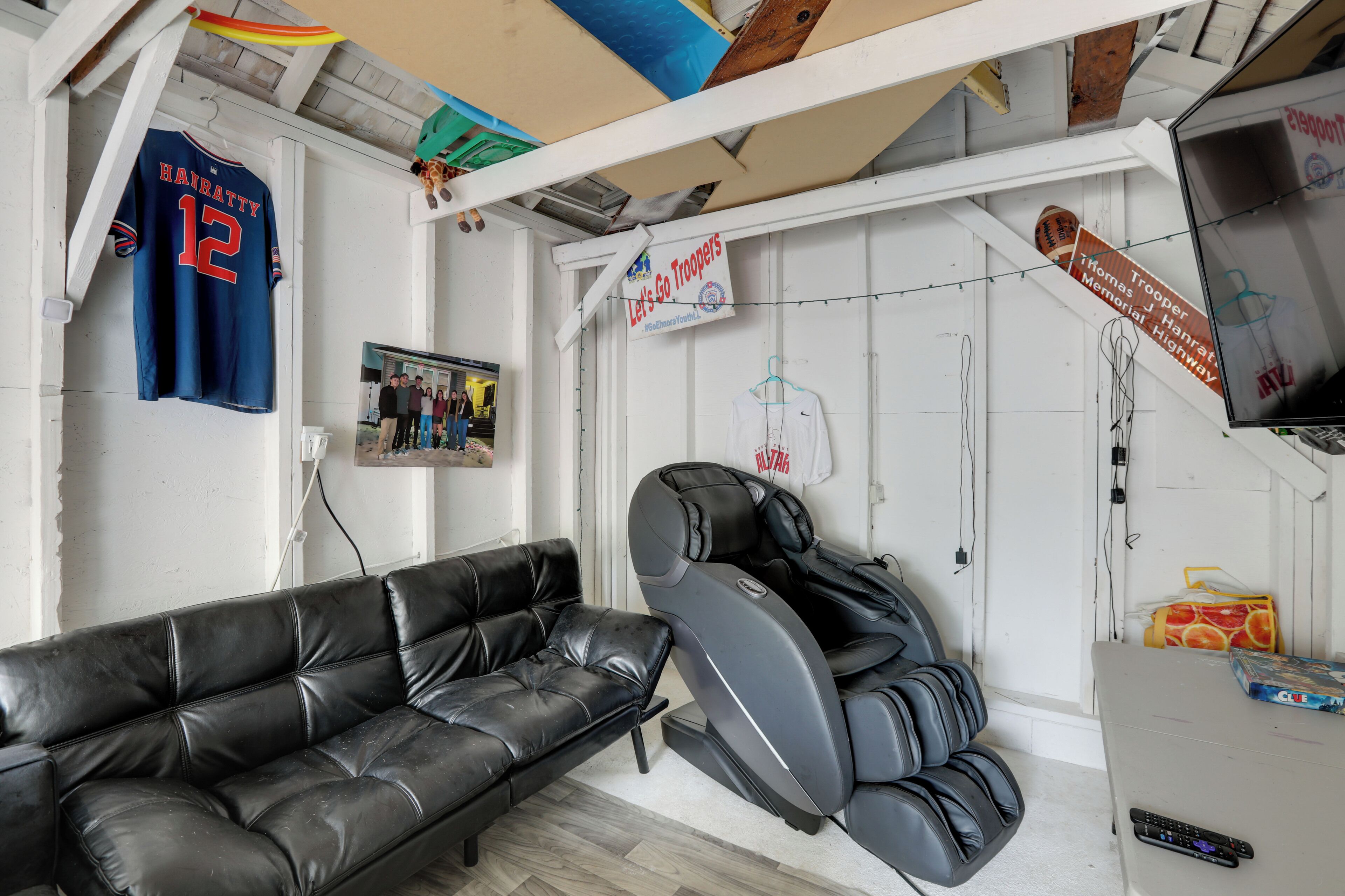 Ein Zimmer mit einer schwarzen Ledersofa, Massagesesseln, einem Fernseher und einem Schild mit der Aufschrift 'Let's Go Troopers'.