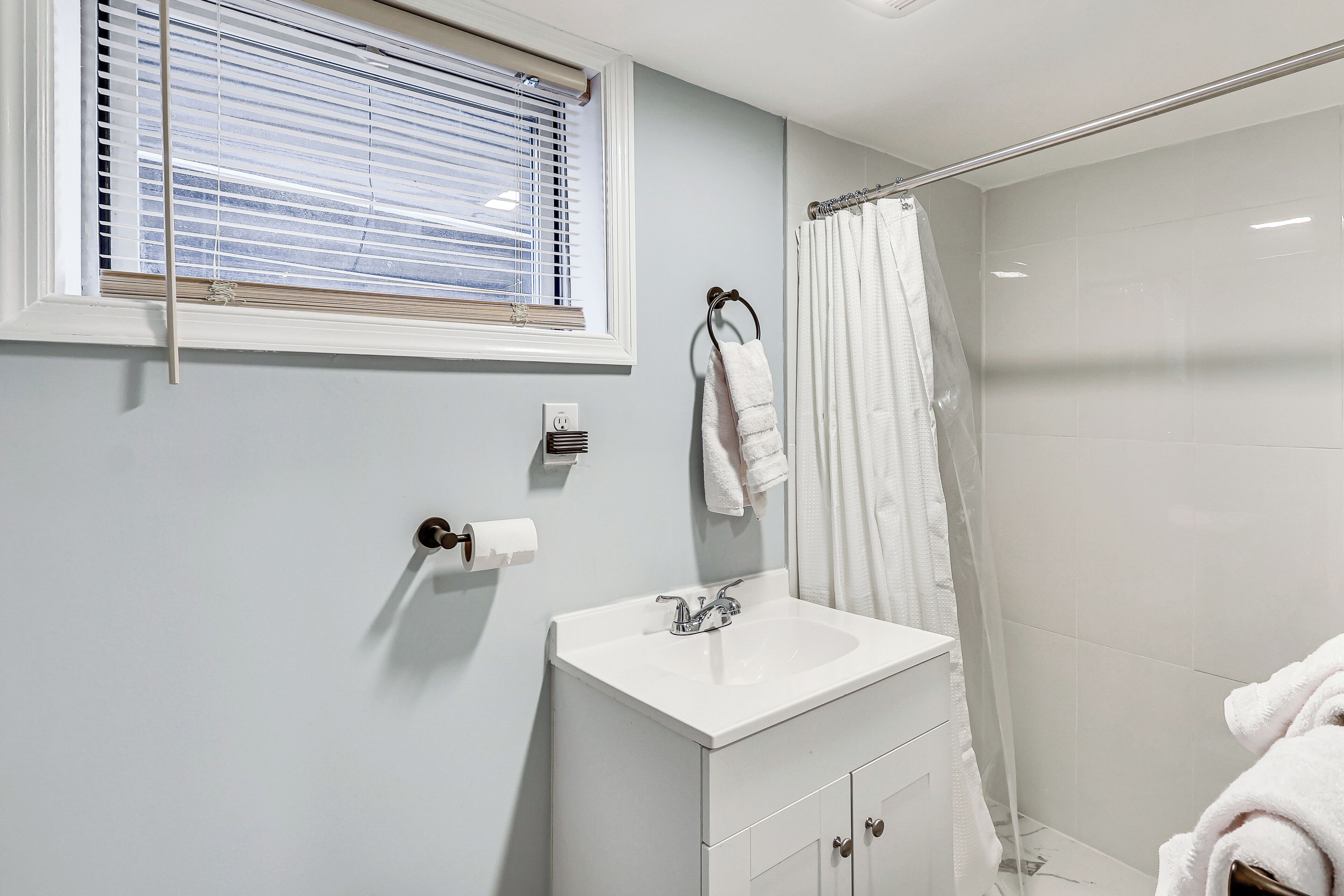 A bathroom with a white sink, a window with blinds, a shower curtain, and a towel rack.