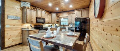 Un intérieur en bois avec une table à manger dressée pour quatre personnes, des placards de cuisine, un four à micro-ondes et une horloge au mur.