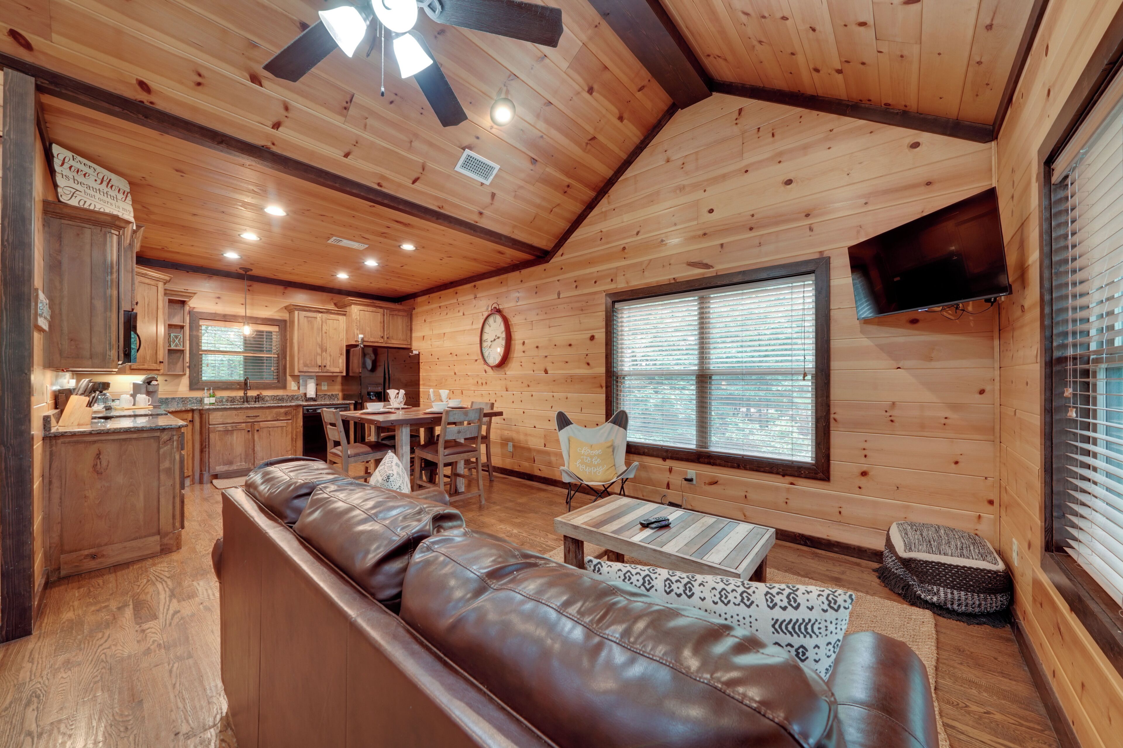 A cabin interior with a wooden ceiling, a dining area, a living room with a sofa, and a kitchen.