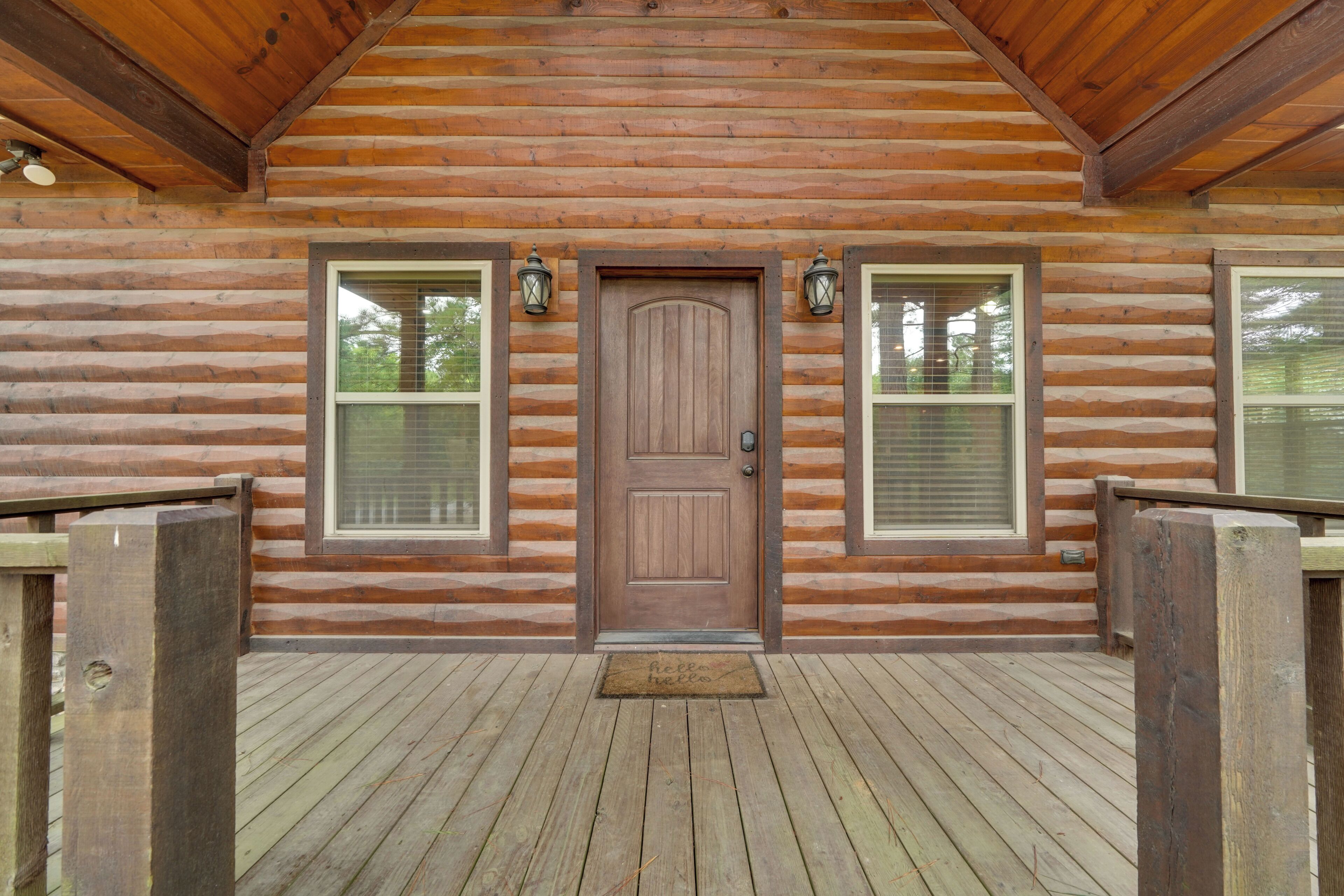 A log cabin with a wooden deck, a central door, and two windows with shutters.