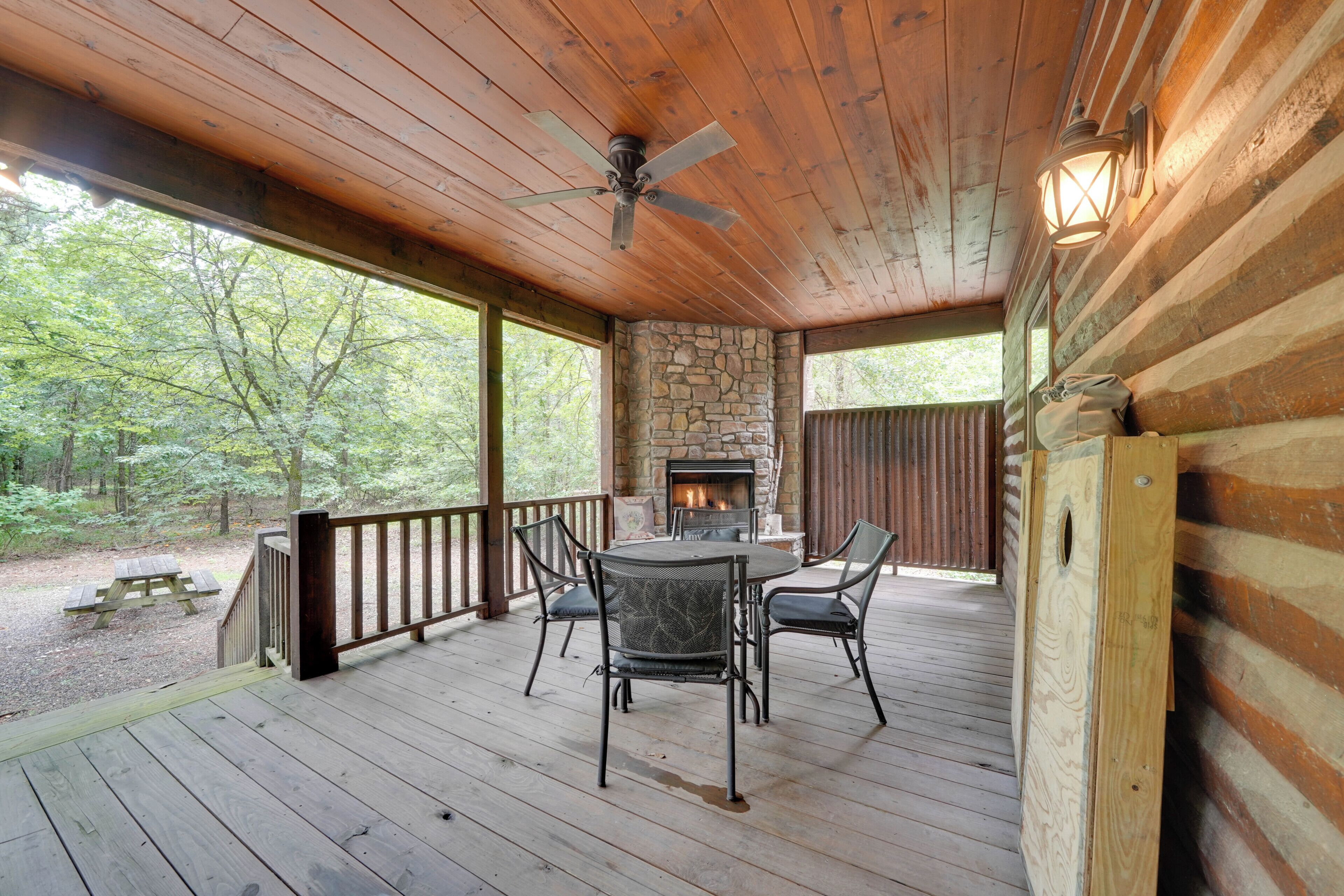 A wooden deck with a stone fireplace, a ceiling fan, and a table with chairs.