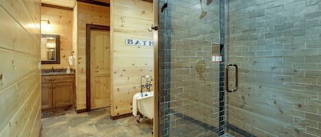 A wooden interior bathroom with a glass shower enclosure, a white bathtub, and a wooden door labeled 'BATH.'