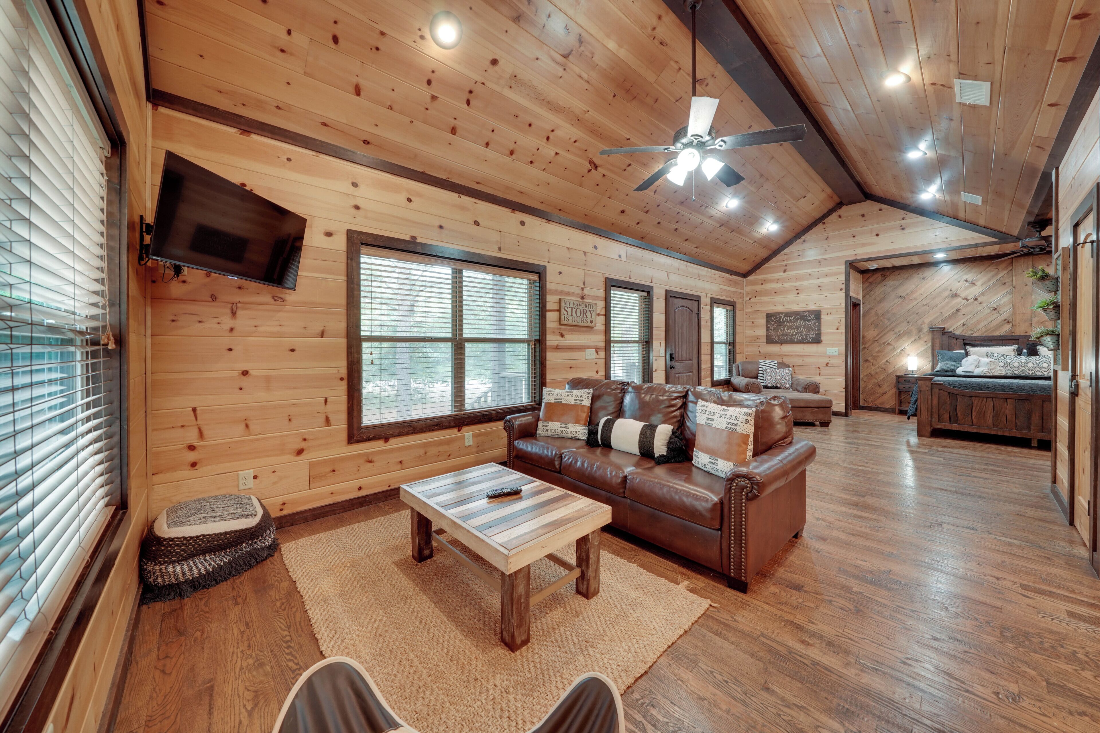 A spacious log cabin interior with a living room, wooden floors, a ceiling fan, and a television mounted on the wall.