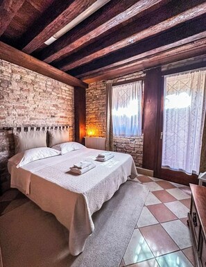Una stanza con un letto grande, pareti in pietra, travi in legno, un camino e una finestra con tende.
