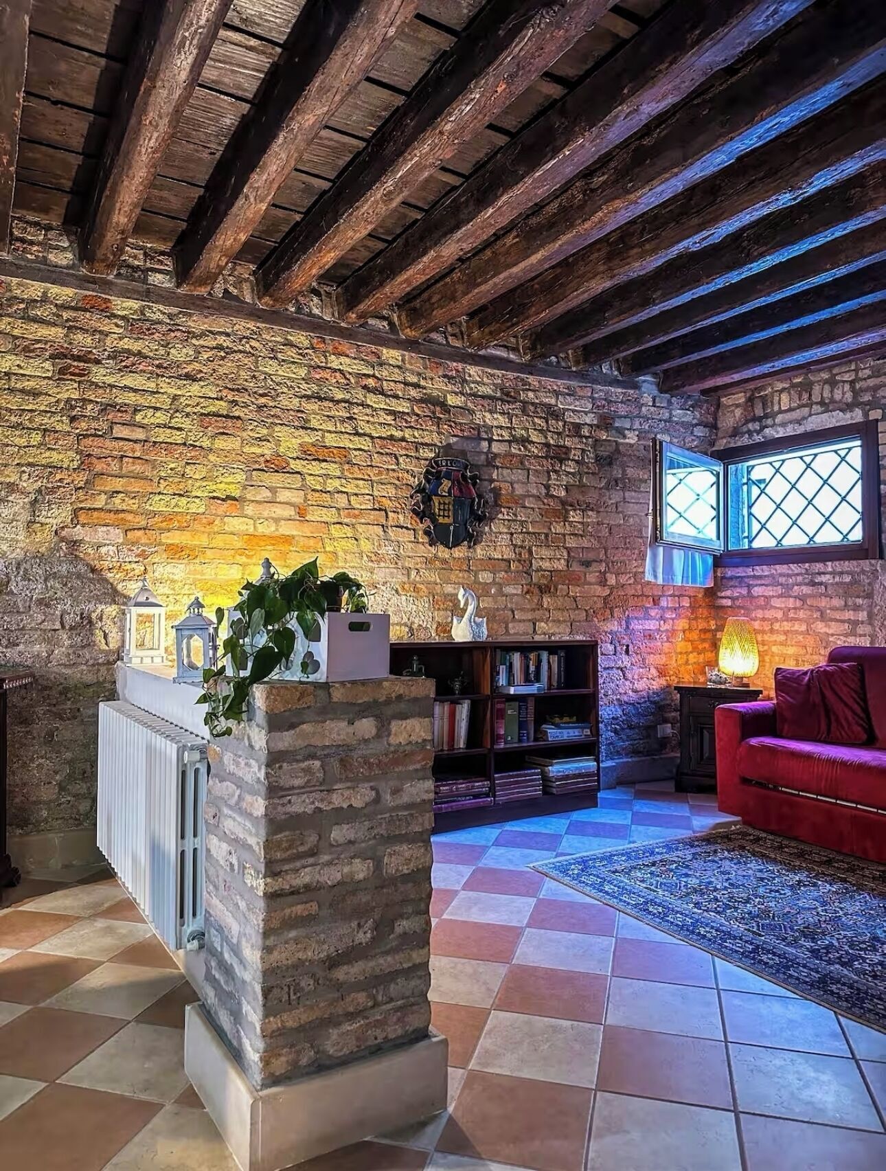 Una stanza rustica con travi a vista in legno, parete in mattoni, una libreria, un divano rosso e un tappeto decorato.