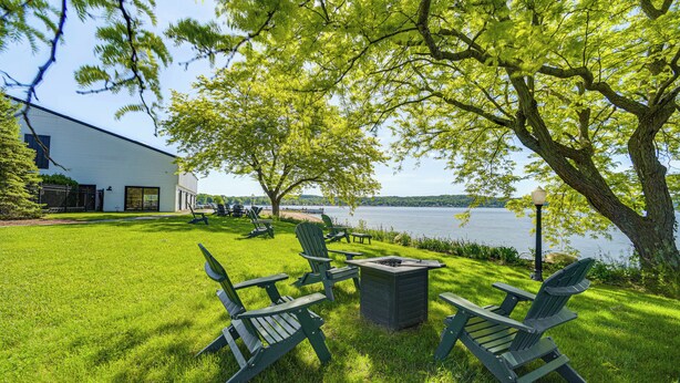 A grassy outdoor area with Adirondack chairs and a fire pit, overlooking a lake and a building. - 4 Mi to Saratoga Course! Resort-style Condo (Saratoga Springs)