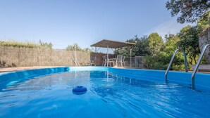 A swimming pool with a diving board, lounge chairs, and a covered seating area.