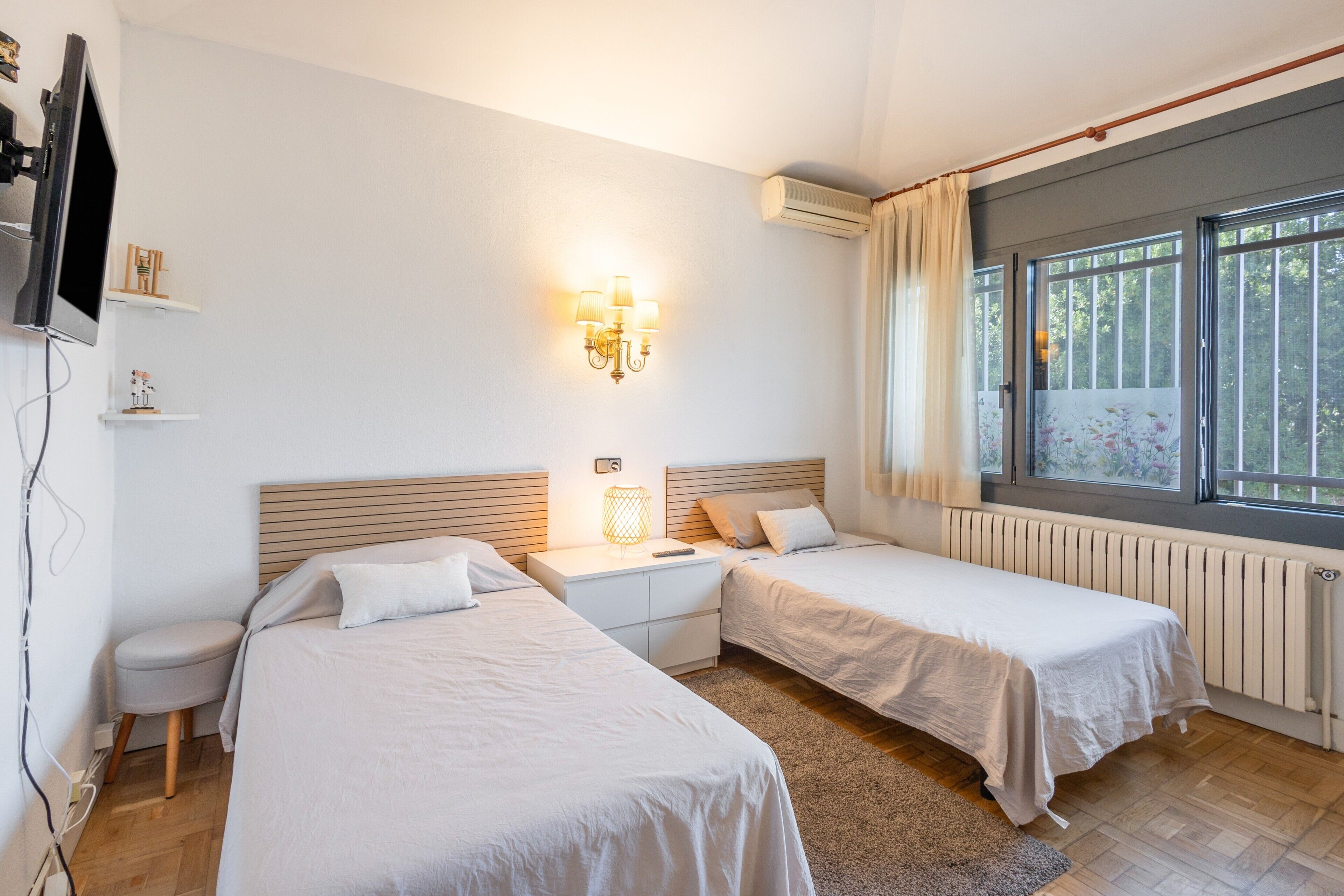 Een hotelkamer met twee bedden, een nachtkastje, een wandtelevisie en een raam met gordijnen.