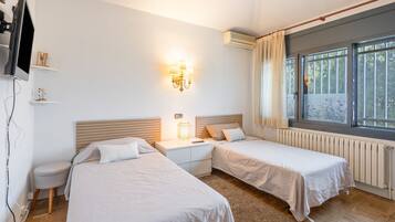 Een hotelkamer met twee bedden, een nachtkastje, een wandtelevisie en een raam met gordijnen.