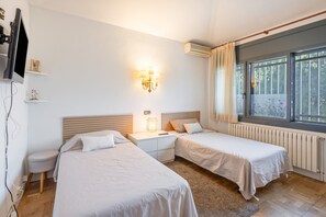 Habitación de hotel con dos camas, una mesita de noche, televisor montado en la pared y una ventana con cortinas.