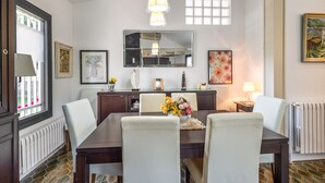 A dining area with a dark wooden table, white chairs, a vase of flowers, a large mirror, and artwork on the walls.