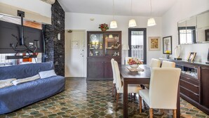 A modern living room with a sofa, dining table, chairs, and a kitchen area with a refrigerator, stove, and cabinets.