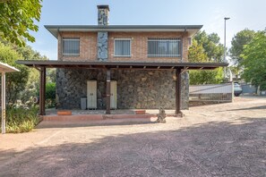 Una casa de piedra de dos pisos con un porche cubierto, una chimenea de piedra y un camino de entrada con portón.