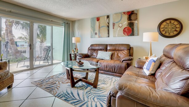 A living room with a leather sofa, a glass coffee table, a wall clock, and abstract art. - Island Walk to Ocean, Dining w/ Boat Dock & Lift! (Jensen Beach)