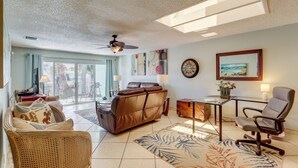 A spacious living area with a sofa, a chair, a table, and a ceiling fan. - Island Walk to Ocean, Dining w/ Boat Dock & Lift! (Jensen Beach)