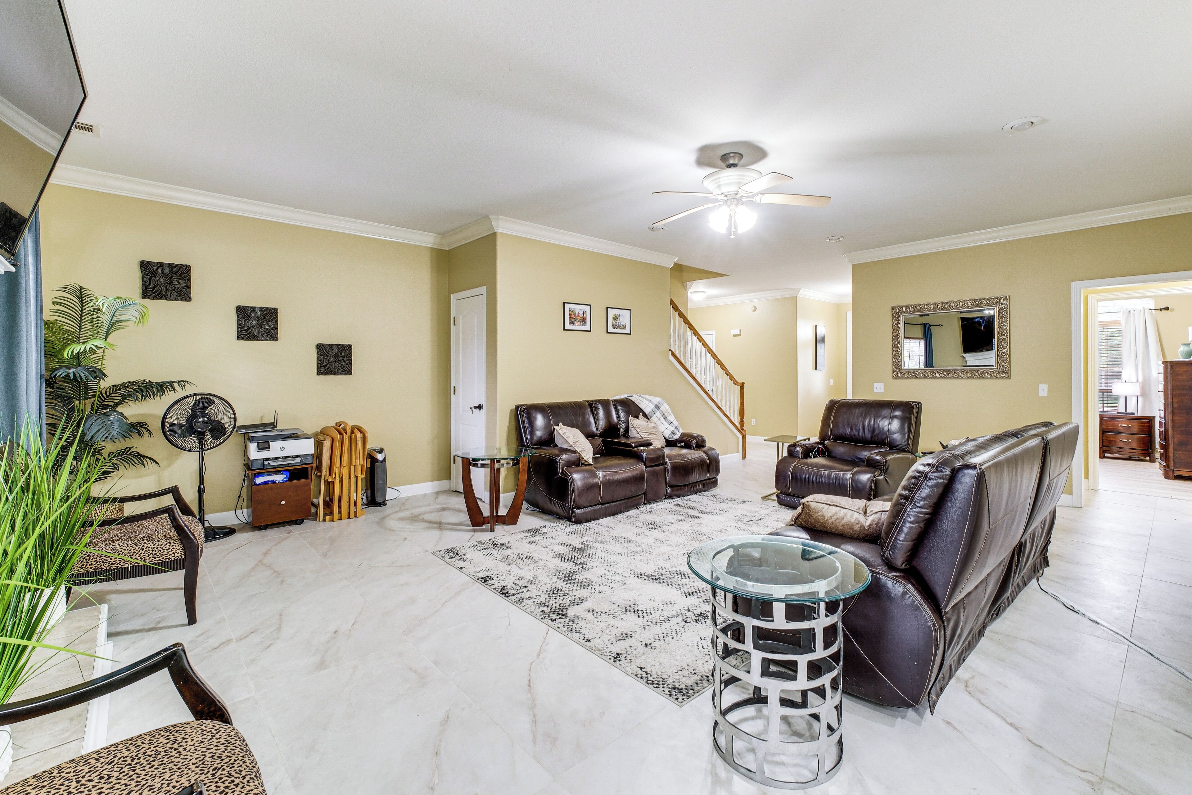 A living room with a sofa, armchairs, a coffee table, a fan, and a staircase.