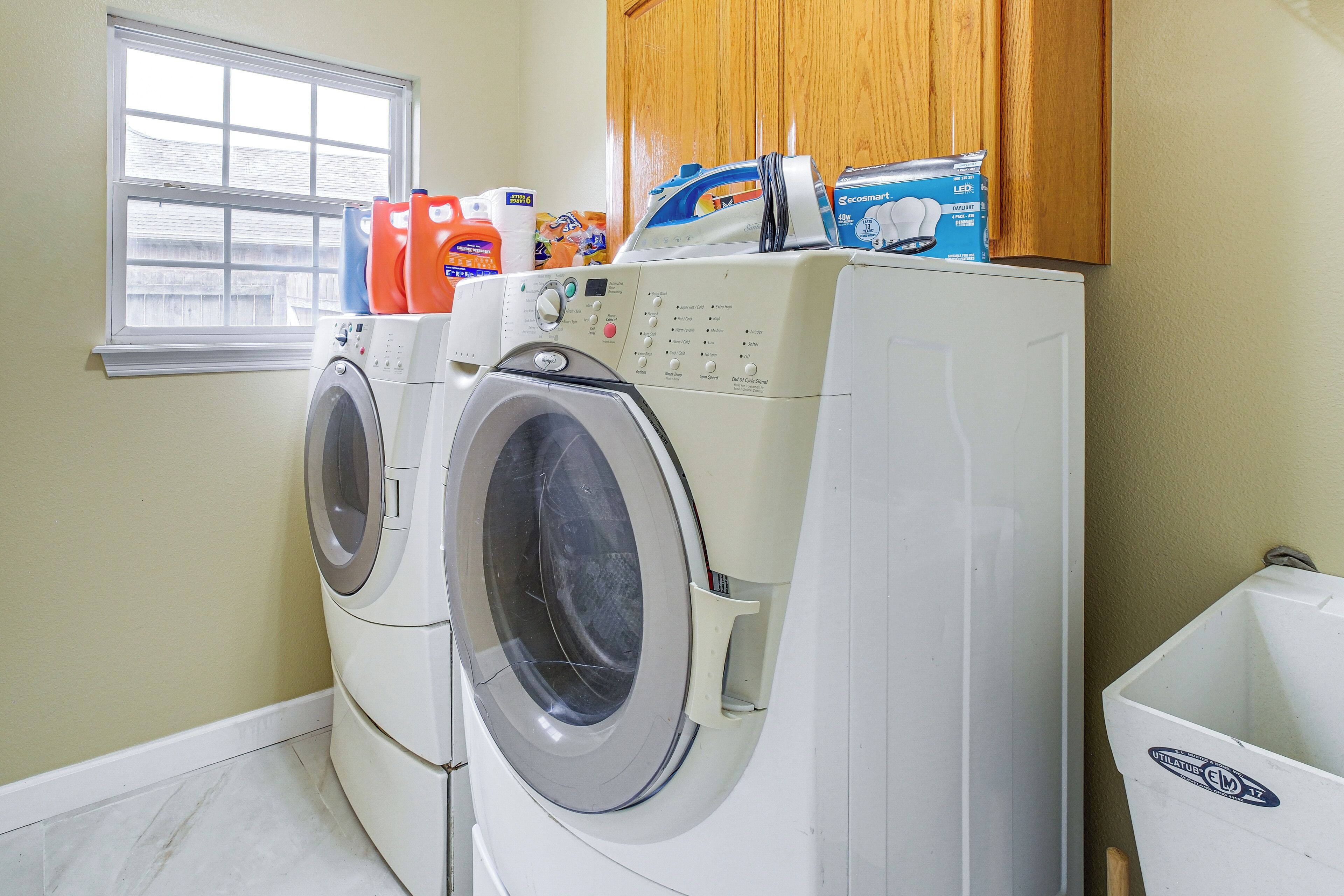 A laundry room with two front-loading washing machines, a dryer, and a utility sink.