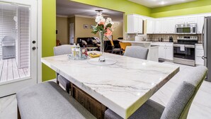 A modern kitchen with white cabinets, a marble island, and a dining area with grey upholstered chairs.