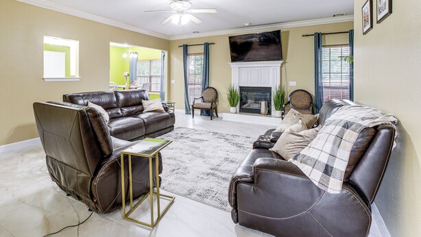 A living room with leather sofas, a fireplace, a television, and a ceiling fan.