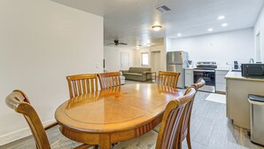 Ein Essbereich mit Holztisch und Stühlen, einem Deckenventilator, Einbauleuchten, einer Küchenzeile mit Geräten und einem Sofa im Hintergrund.