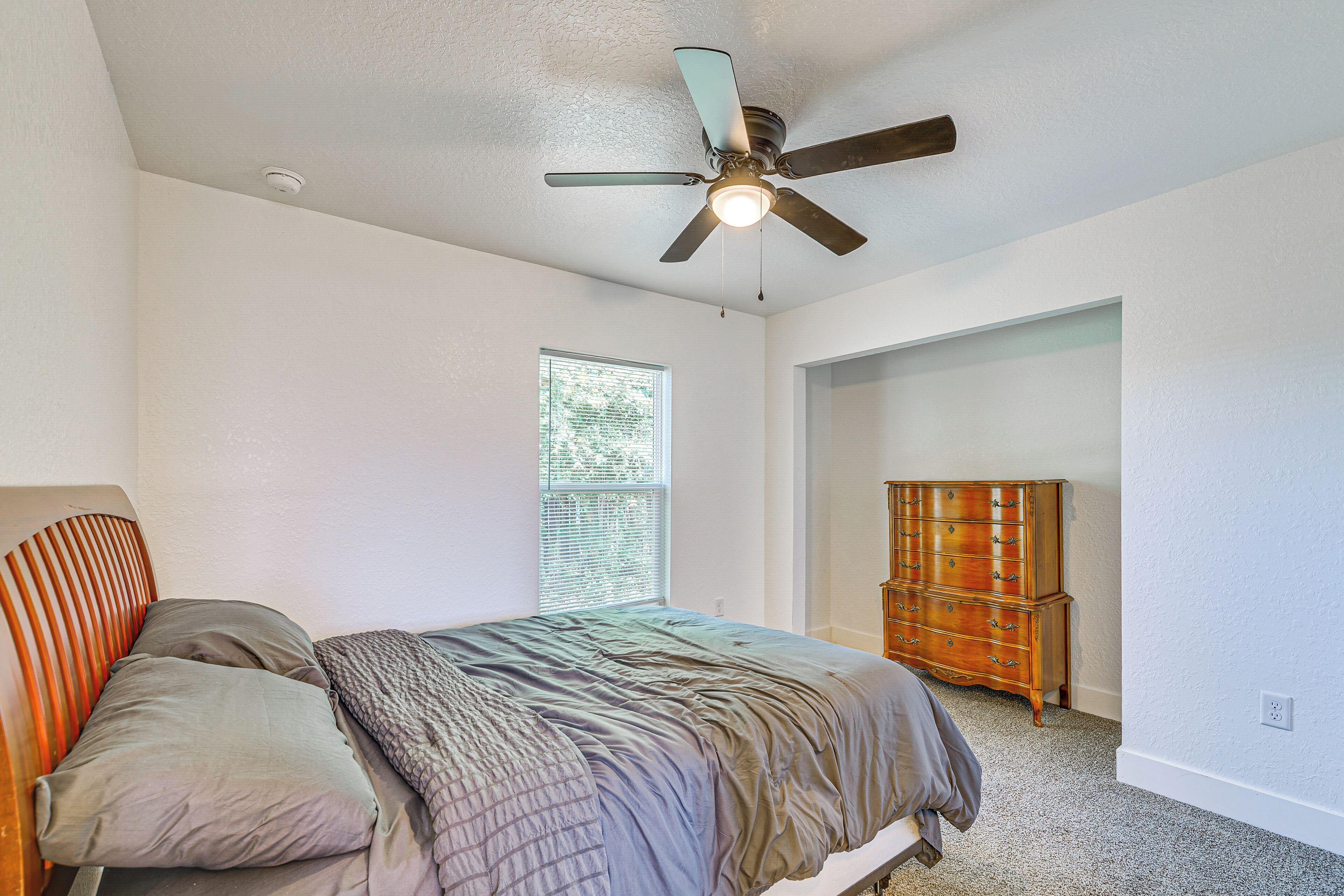 Une chambre à coucher avec un lit, un ventilateur de plafond, une commode et une fenêtre.