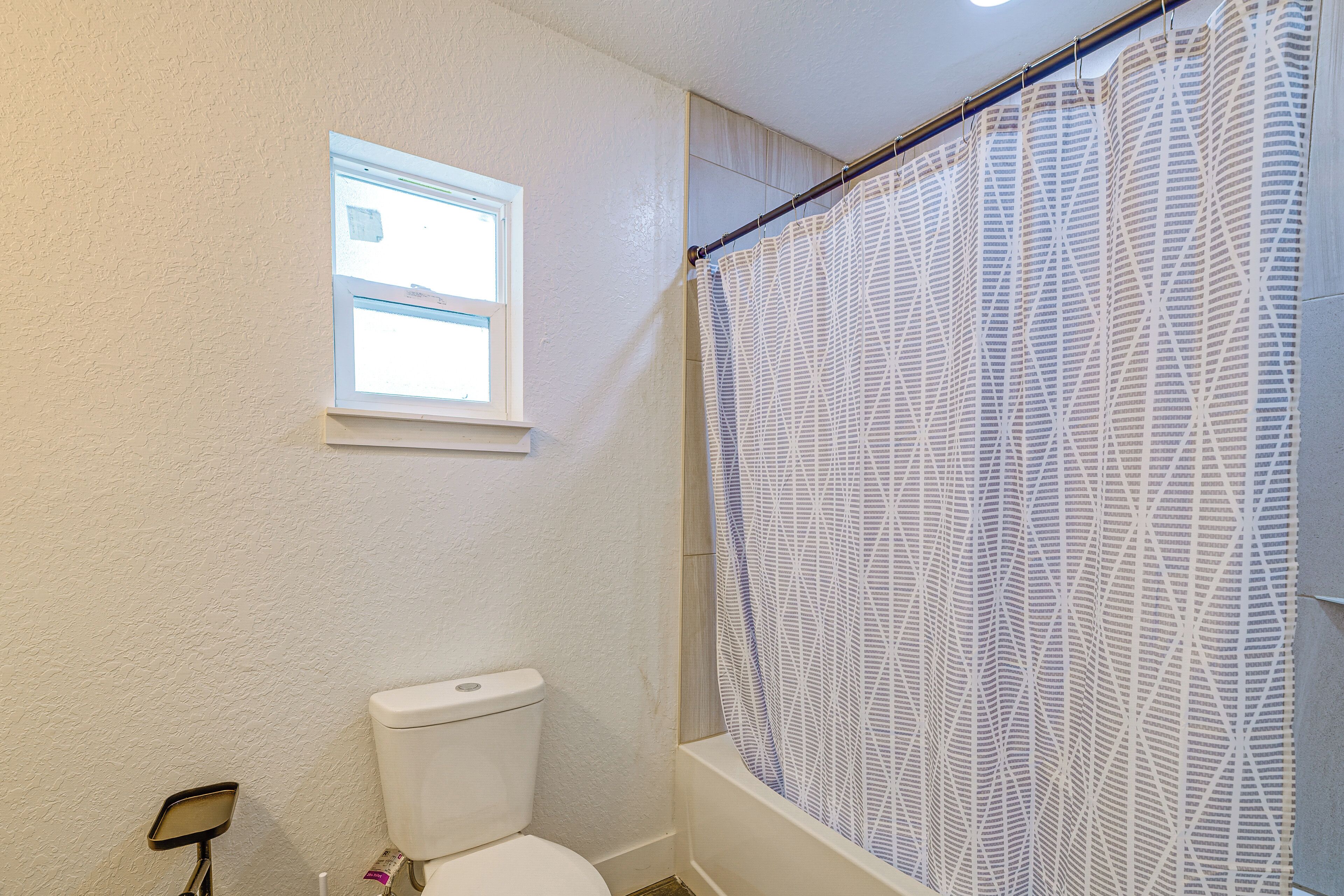 A bathroom with a toilet, a window, and a shower curtain.