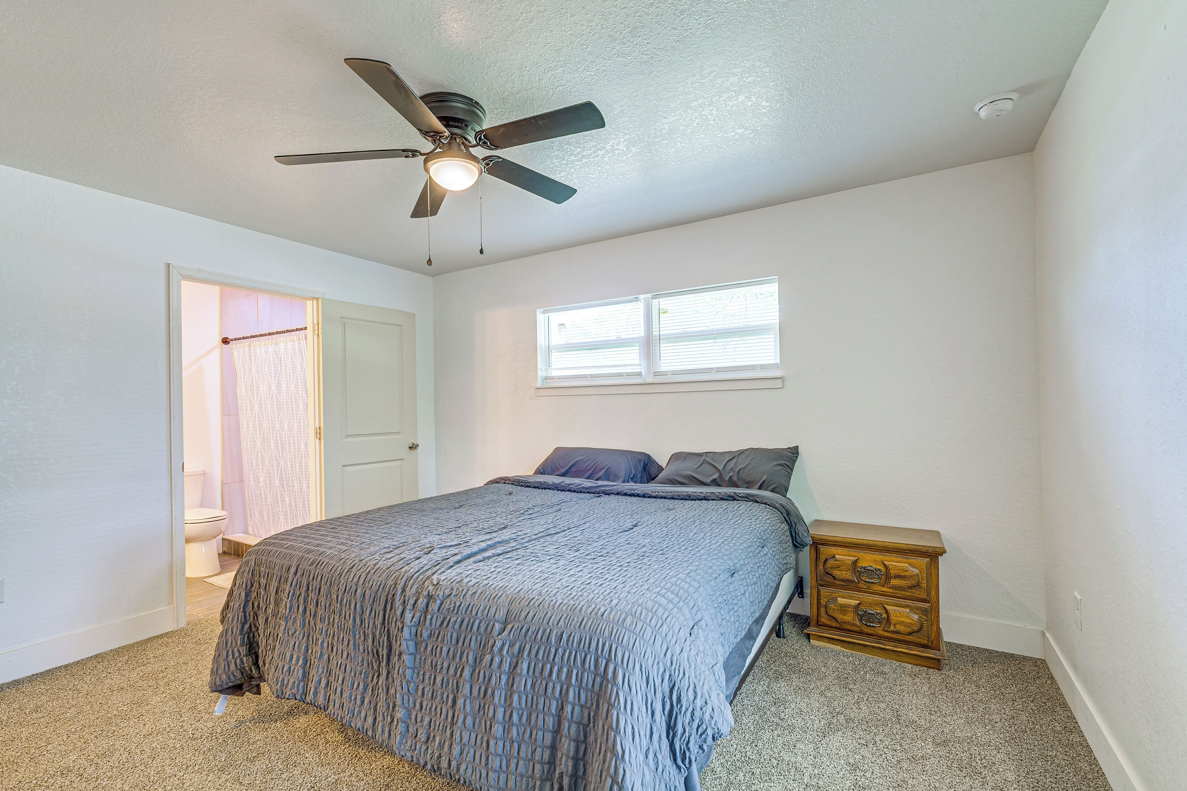 A bedroom with a bed, a ceiling fan, a window, and a nightstand.