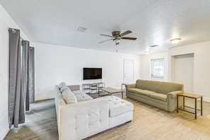 A living room with a sectional sofa, a tan couch, a coffee table, a TV, and a ceiling fan. - 6 Mi to Rainbow Springs: Dunnellon Retreat! (Dunnellon)