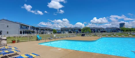 A swimming pool with lounge chairs, a fenced area, and a building with a flat roof in the background.