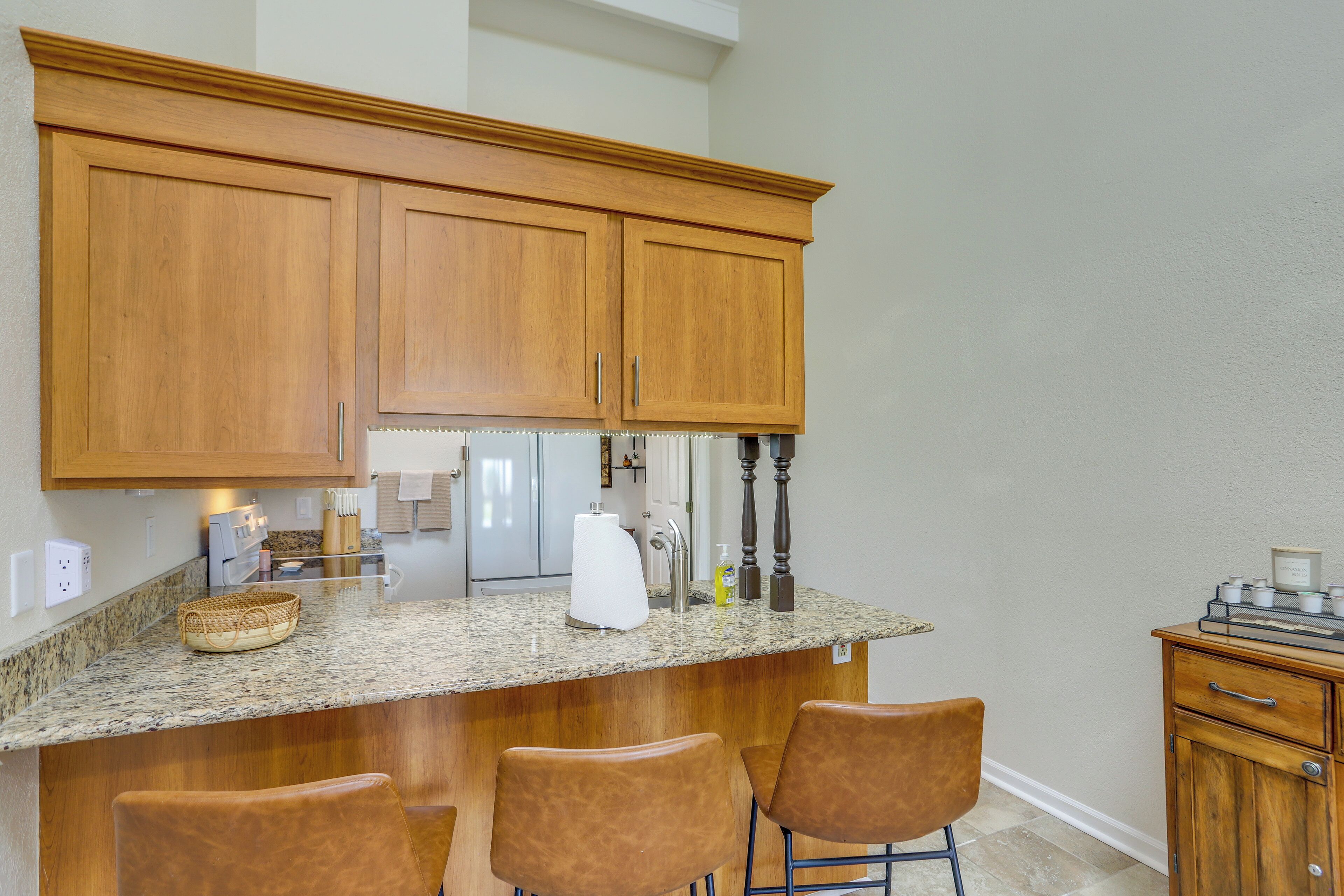 A kitchen with wooden cabinets, a granite countertop, and three bar stools.