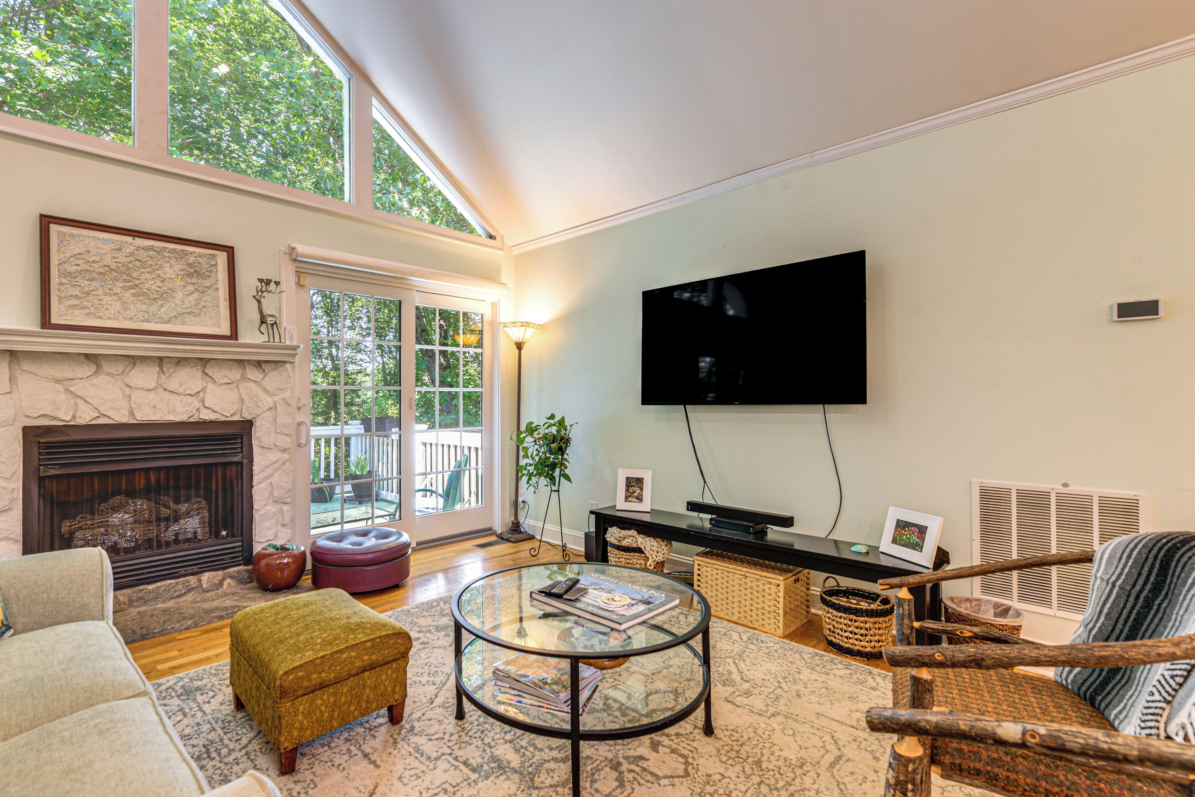 A living room with a fireplace, a television, a glass coffee table, and a view of the outdoors.