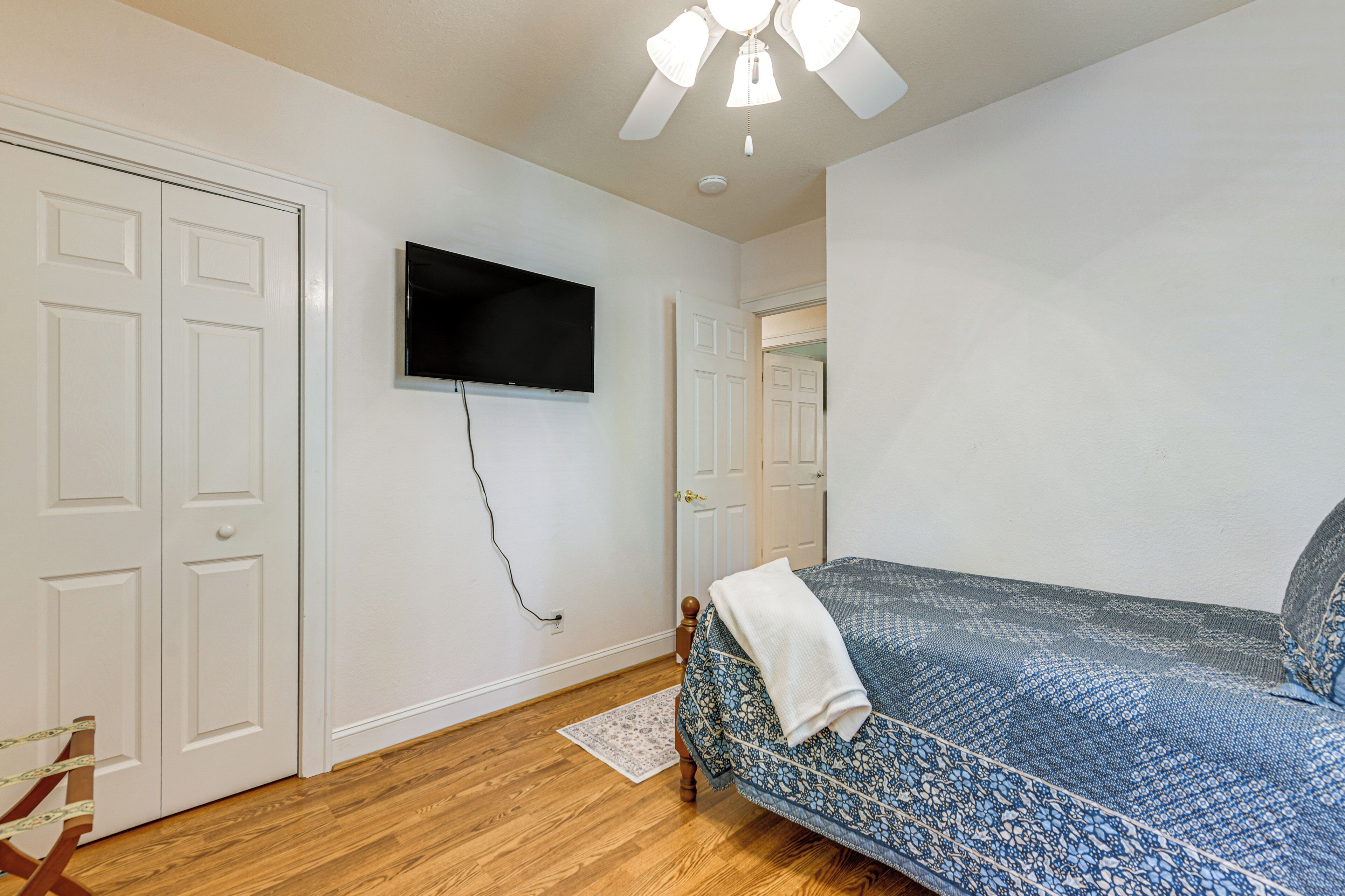 A bedroom with a bed, a television mounted on the wall, and a ceiling fan.