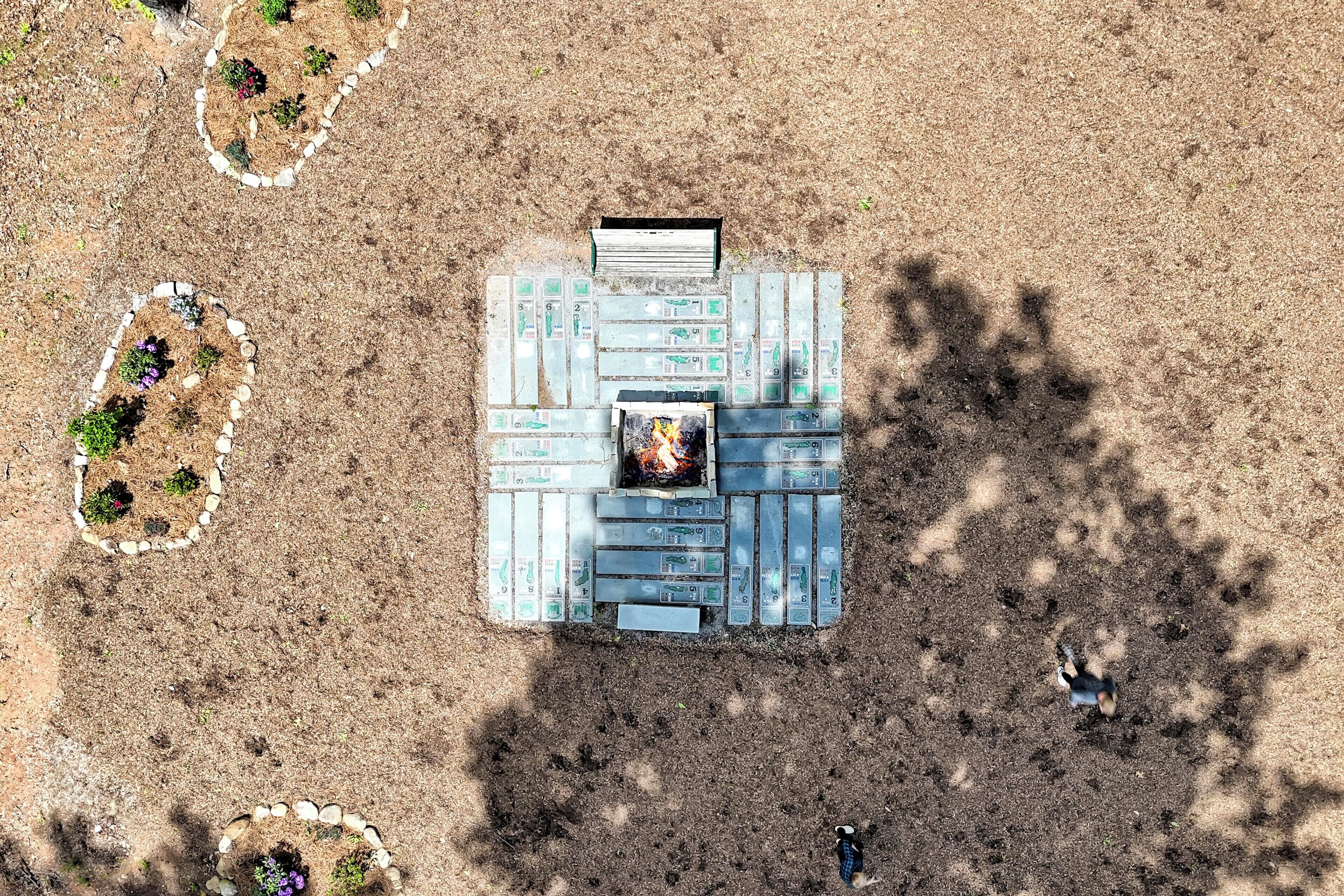 An aerial view of a campsite with a fire pit, surrounded by garden beds with plants.