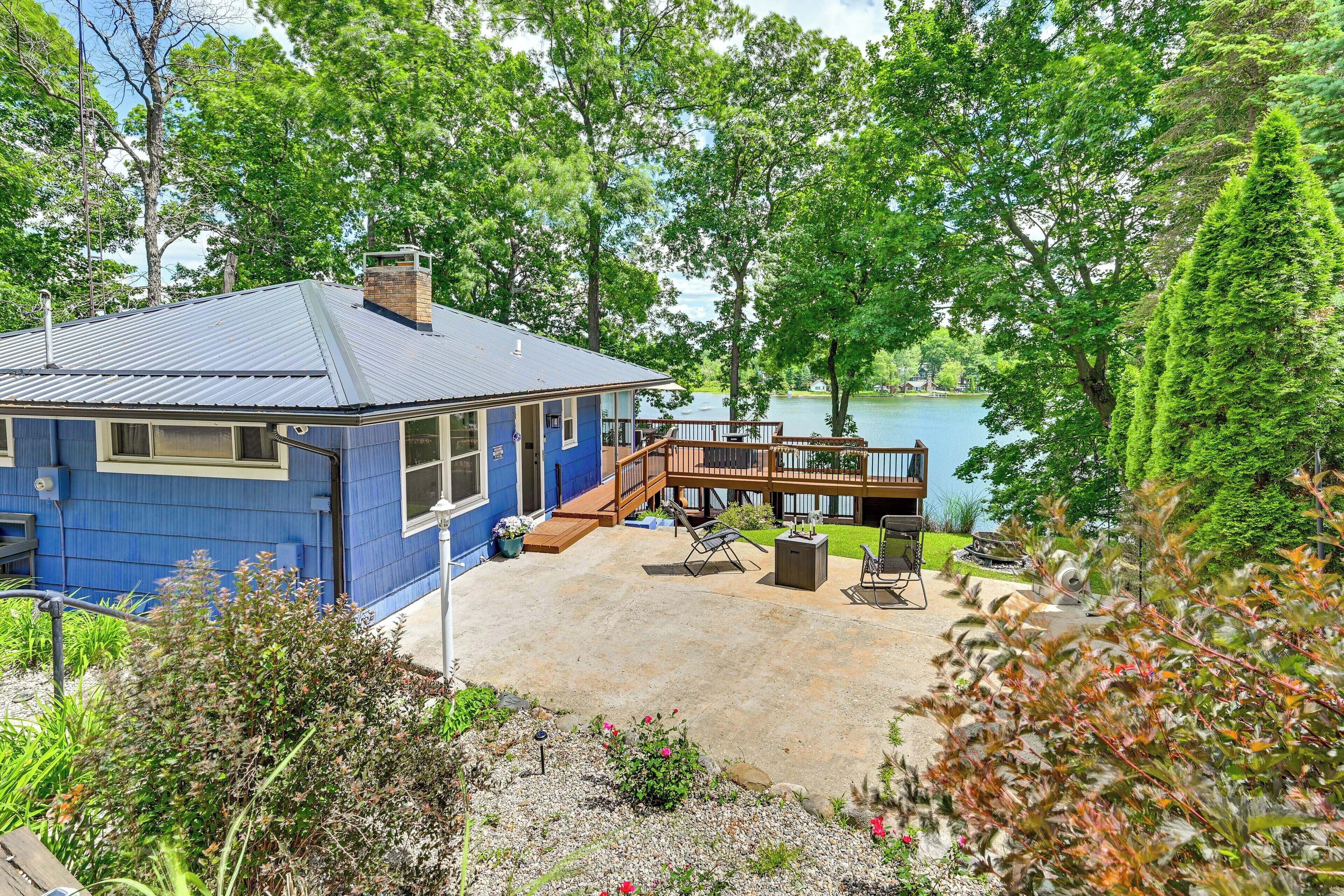 A blue house with a deck overlooking a lake, surrounded by trees.