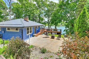 A blue house with a deck overlooking a lake, surrounded by trees.
