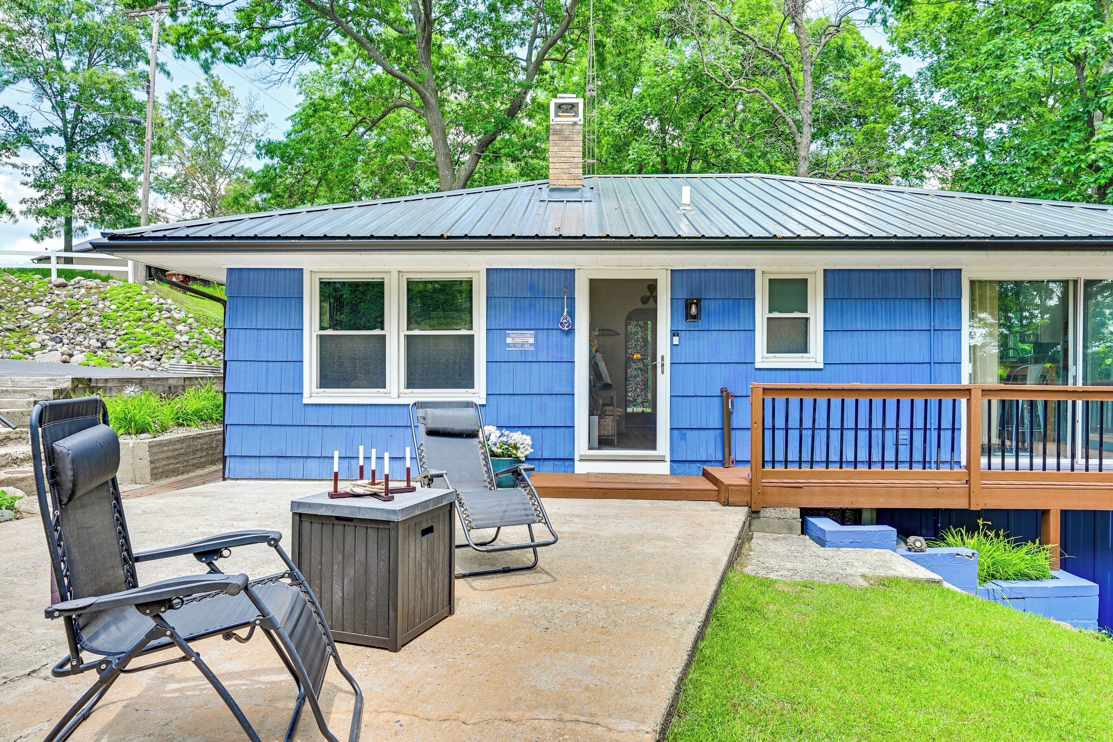 A blue house with a deck, a patio with chairs, and a grill.