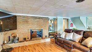 Una sala de estar con chimenea de ladrillo, sofá de cuero, piso de madera y televisor montado.