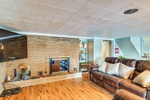 Una sala de estar con chimenea de ladrillo, sofá de cuero, piso de madera y televisor montado.
