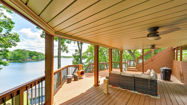 Una terraza de madera con jacuzzi, mobiliario exterior y vista a un lago.