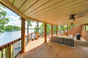 Una terraza de madera con jacuzzi, mobiliario exterior y vista a un lago.