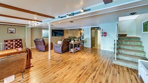 Amplia sala de estar con suelo de madera, chimenea, escalera y comedor con mesa y sillas de madera.
