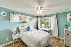 A bedroom with a bed, bedside table, nightstand, ceiling fan, window with curtains, and a desk with a chair.