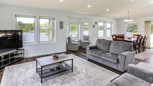 A living room with a TV, sofa, coffee table, and large windows overlooking a body of water. - Modern Waterfront Home w/ Dock & Views in Deale (Deale)
